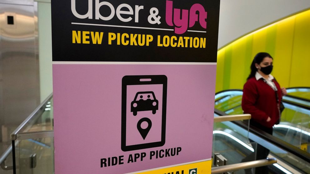 FILE - In this Feb. 9, 2021 file photo, a passer-by walks past a sign offering directions to an Uber and Lyft ride pickup location at Logan International Airport, in Boston. Ride-hailing companies Uber and Lyft said Friday, Sept. 3, 2021 they will co