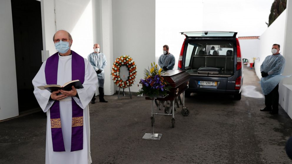 A priest says a few words during a brief ceremony outdoors before the cremation of a COVID-19 victim at a cemetery in Alcabideche, outside Lisbon, Wednesday, Feb. 3, 2021. Portugal is facing a pandemic surge that has made it the world's worst-hit cou
