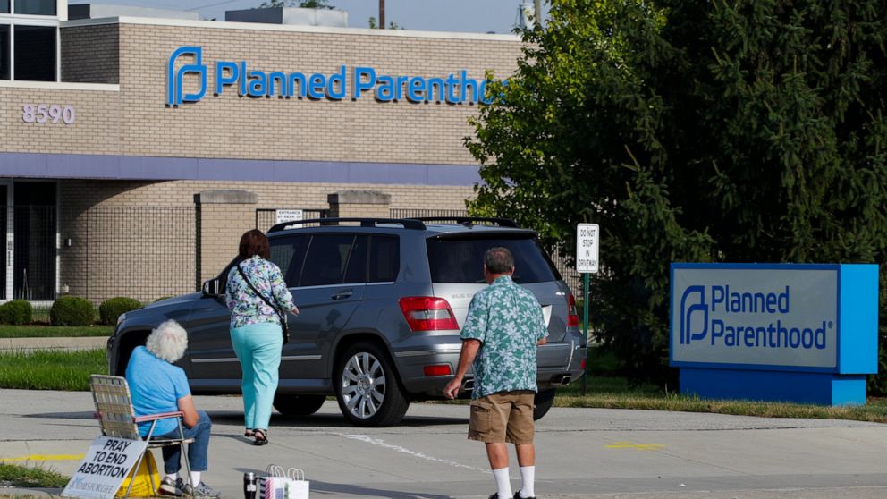 FILE - In this Aug. 16, 2019 file photo, abortion protesters attempt to handout literature as they stand in the driveway of a Planned Parenthood clinic in Indianapolis. A federal judge has blocked a new Indiana law that would require doctors to tell 