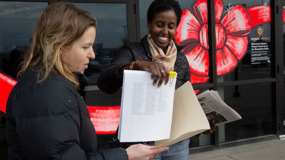 In this Wednesday, Nov. 20, 2019 photo, from left, Mary Blitzer, of the Sierra Club, gives a petition of over 23,000 signatures to Amira Adawe of the Beautywell Project as they deliver it to the Amazon Fulfillment Center in Shakopee, Minn. The two no