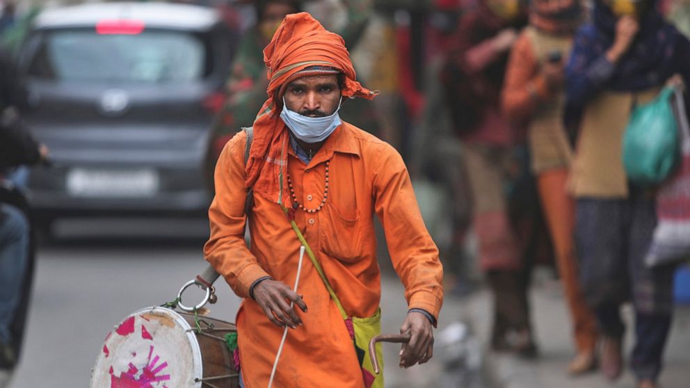 A man wears his face mask below his nose and walks in a market area with a traditional percussion instrument in Jammu, India, Saturday, Jan.15, 2022. It’s mandatory to wear a mask in India. And police are out on the streets, watching people to make s