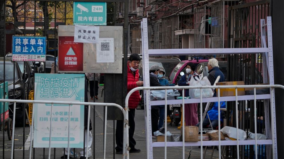 FILE - Residents wearing face masks chat with each other near the barriers set up in a locked down neighborhood as part of COVID-19 controls in Beijing, Wednesday, Nov. 23, 2022. (AP Photo/Andy Wong, File)