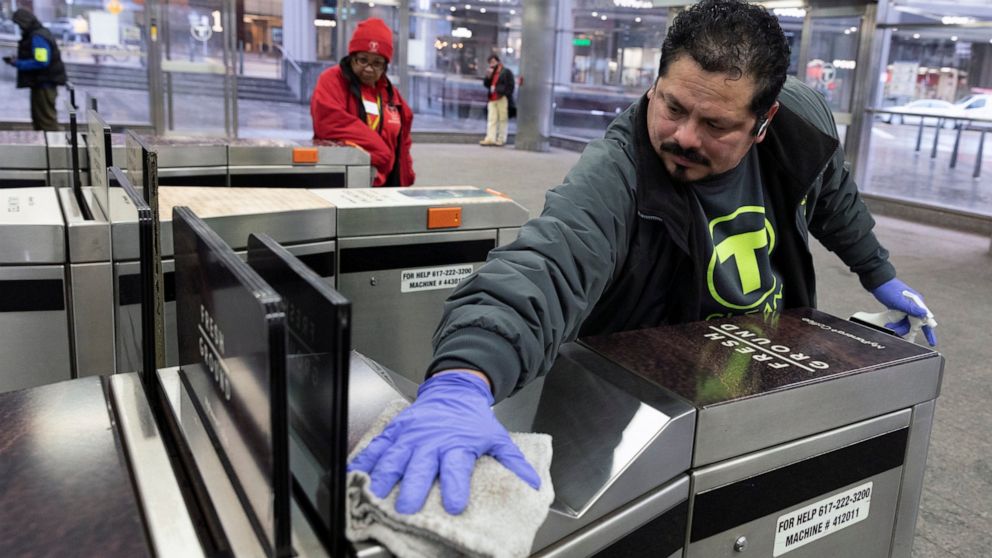 FILE - In this March 13, 2020 file photo, a worker disinfects a turnstile at the Government Center transit stop, in Boston. As the global viral pandemic grows, the need for cleaning and disinfecting has surged. Cleaners and domestic workers are essen