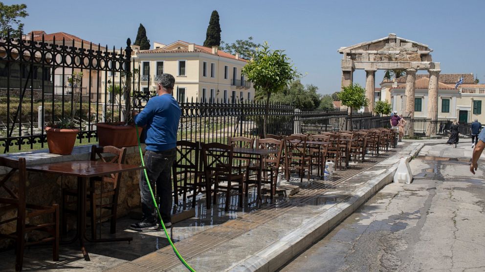 A man cleans with a water hose outside a traditional restaurant in front of the Roman Agora Gate, in Plaka, district of Athens, Friday, April 30, 2021. COVID-19 restrictions will be relaxed in Greece for Orthodox Easter on Sunday, allowing cafe and r