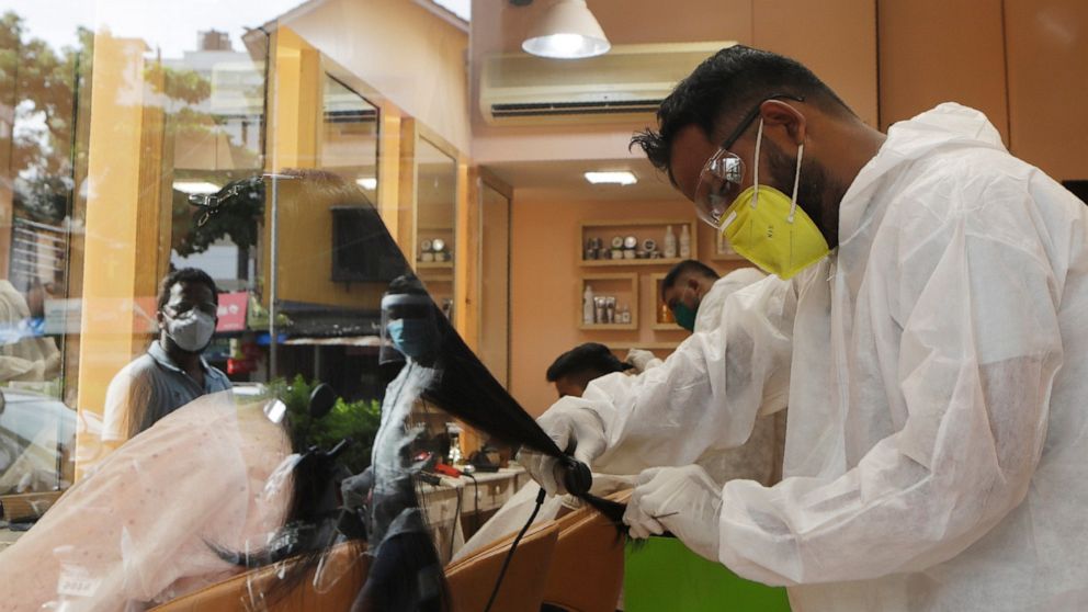 A hairstylist works on a customer in Mumbai, India, Sunday, June 28, 2020. India is the fourth hardest-hit country by the COVID-19 pandemic in the world after the U.S., Russia and Brazil. (AP Photo/Rajanish Kakade)