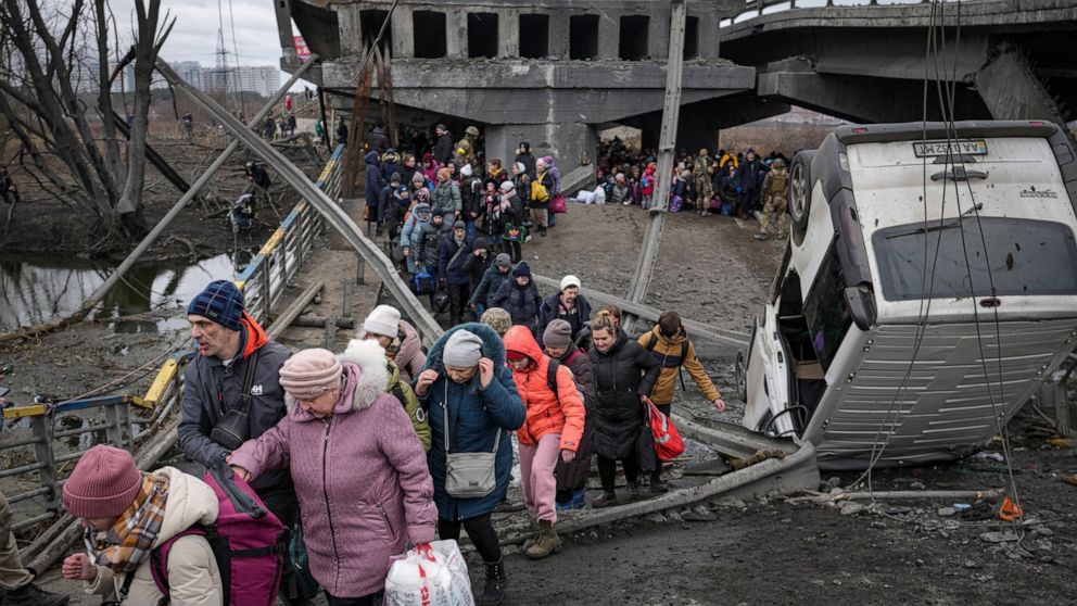 FILE - People cross the Irpin river on an improvised path under a bridge, that was destroyed by Ukrainian troops designed to slow any Russian military advance, while fleeing the town of Irpin, Ukraine, Saturday, March 5, 2022. Member countries of the