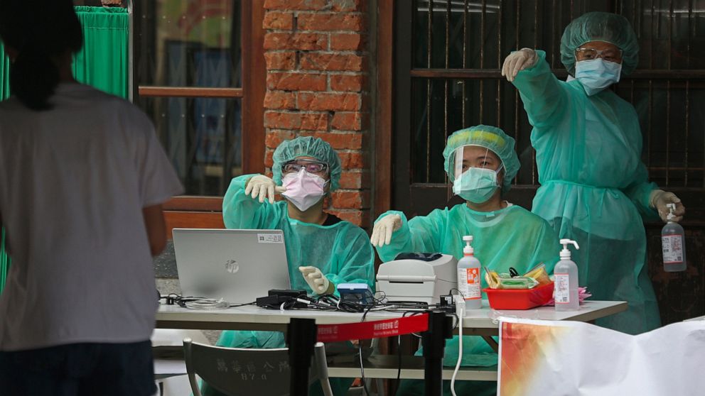 FILE - In this May 18, 2021, file photo, medical personnel wearing protective gear, guide people at a rapid coronavirus testing center after the infection alert rose to level 3 in Taipei, Taiwan. After a year of success, Taiwan is struggling with its