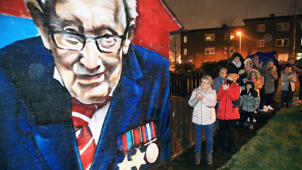 Local residents join a national clap beside a mural of Captain Sir Tom Moore in East Belfast, Northern Ireland, Wednesday, Feb. 3, 2021. Captain Moore passed away Tuesday after being treated with Covid-19 and was known for his achievements raising mi