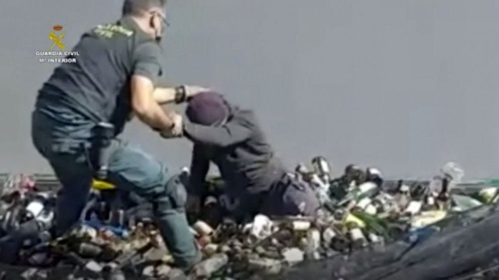 In this image taken from video made available by the Guardia Civil, an officer of the Guardia Civil helps a man out from under glass bottles in a container in Melilla, Spain, Friday Feb. 19, 2021. Spanish authorities say they have found and rescued 4