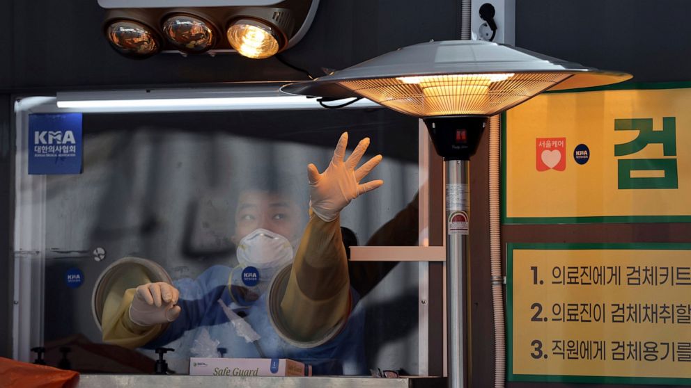 A medical worker wearing protective gear tries to warm his hand in the sub-zero temperatures at a coronavirus testing site in Seoul, South Korea, Thursday, Dec. 31, 2020. (Kim In-chul/Yonhap via AP)