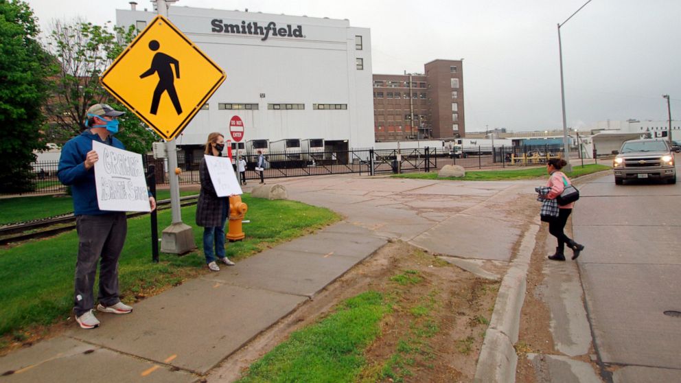 FILE - In this May 20, 2020, file photo, residents cheer and hold thank you signs to greet employees of a Smithfield pork processing plant as they begin their shift in Sioux Falls, S.D. Workers at the South Dakota meatpacking plant that became a coro