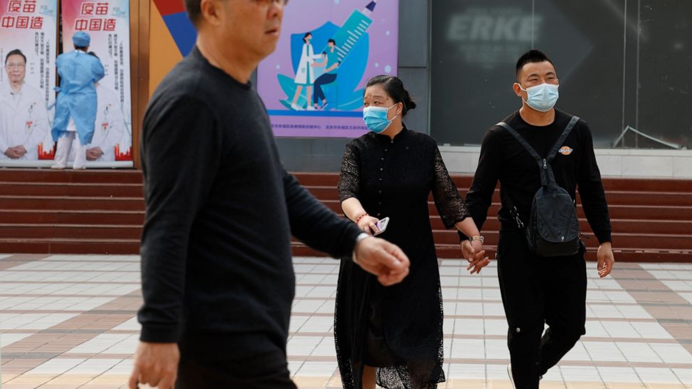 Chinese residents, some wearing masks, pass by a coronavirus vaccination center in Beijing Friday, April 9, 2021. In a rare admission of the weakness of Chinese coronavirus vaccines, the country's top disease control official says their effectiveness