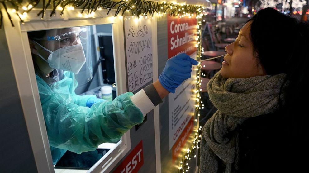 FILE -- A test center employee performs a coronavirus test as she stands in the 'Kurfuerstendamm (Ku'damm)' shopping road in Berlin, Germany, Tuesday, Dec. 21, 2021. Germany's governing coalition is arguing over whether remaining coronavirus restrict