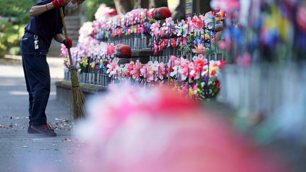 An employee wearing a protective mask to help curb the spread of the coronavirus sweeps near pinwheels whirl in the breeze at rows of small stone statues of "jizo" representing the unborn children at a temple in Tokyo Thursday, Oct. 29, 2020. The Jap