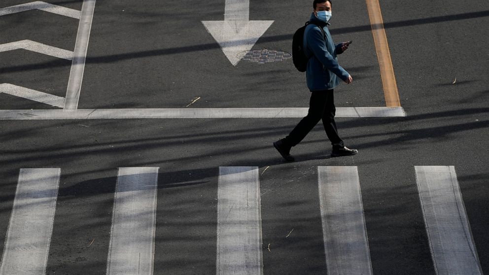 A man wearing a face mask walks across a street in Beijing, Wednesday, Nov. 16, 2022. Chinese authorities locked down a major university in Beijing on Wednesday after finding one COVID-19 case as they stick to a "zero-COVID" approach despite growing 