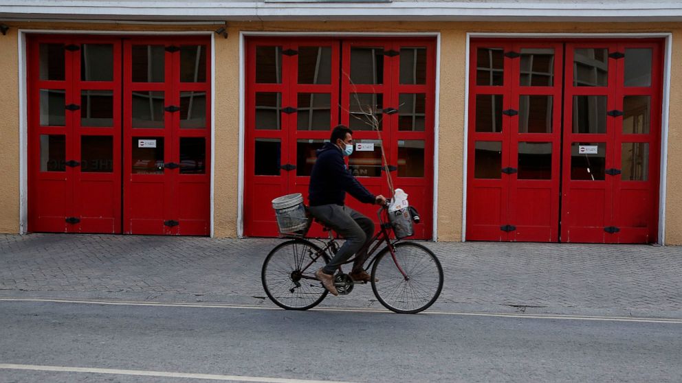 A man wears a face mask on his bicycle in central capital Nicosia, Cyprus, Wednesday, Jan. 27, 2021. Cyprus' health minister Constantinos Ioannou said that the first to re-open as of Feb. 1st will be hair and beauty salons followed a week later by re