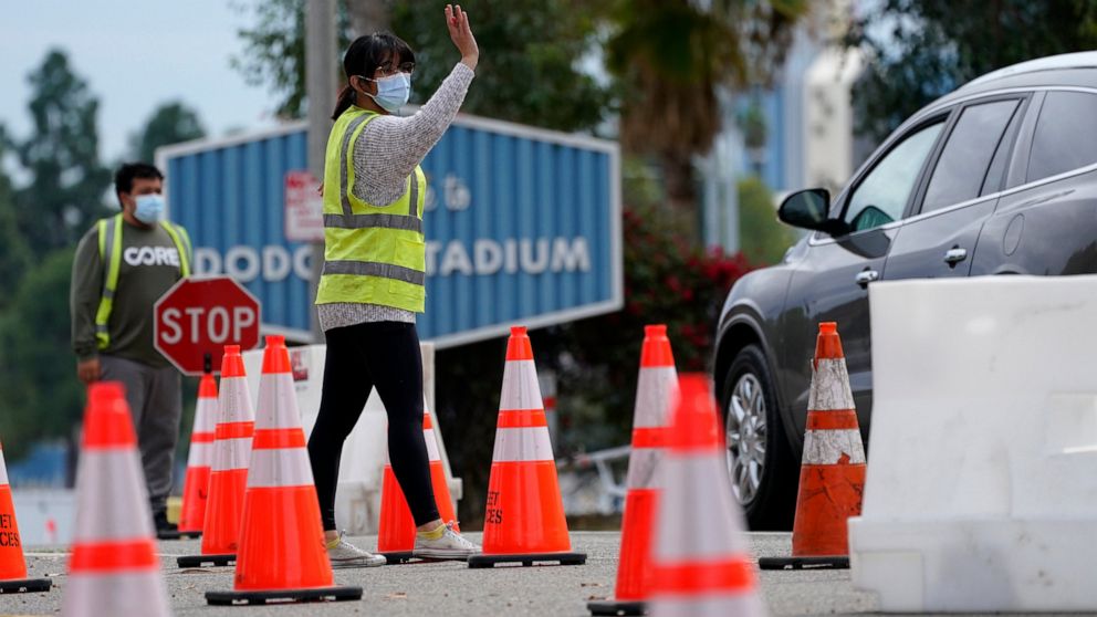 Cars are waved in as people arrive at the Dodger Stadium parking lot to receive the COVID-19 vaccine Monday, Feb. 1, 2021, in Los Angeles. One of the largest vaccination sites in the nation temporarily shut down Saturday because dozen of protesters b