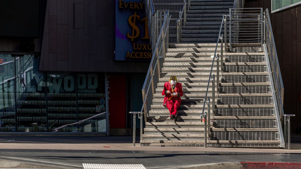 A street performer dressed as the Joker sits to eat his lunch on the steps of the closed Madame Tussauds Hollywood wax museum, a tourist destination on Hollywood Boulevard in Los Angeles on Tuesday, March 24, 2020. (AP Photo/Damian Dovarganes)