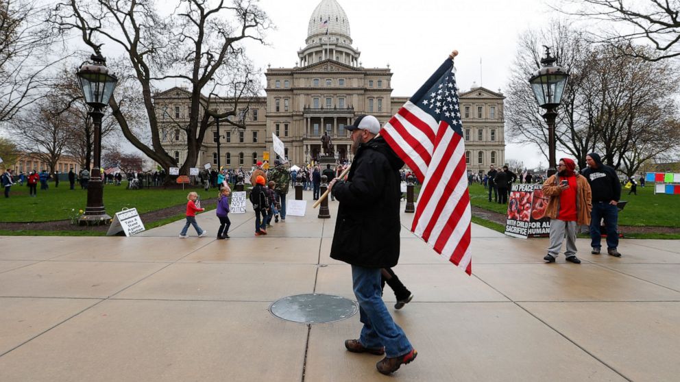 A protester carries an American flag at the State Capitol in Lansing, Mich., Thursday, April 30, 2020. Hoisting American flags and handmade signs, protesters returned to the state Capitol to denounce Gov. Gretchen Whitmer's stay-home order and busine