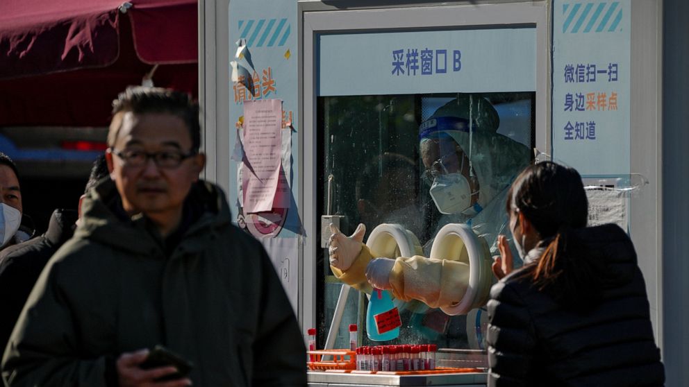 A worker in protective gear disinfects his gloves as residents get their routine COVID-19 throat swabs despite authorities starting to ease some of the anti-virus controls in Beijing, Thursday, Dec. 8, 2022. China is the last major country still tryi
