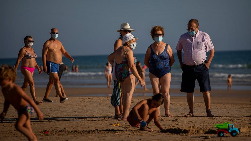 People wearing face masks stay at the beach in Barbate, Cadiz province, south of Spain, on Saturday, July 25, 2020. Ministers are set to remove Spain from the Government's list of safe countries to travel to after the European country saw a rise in C