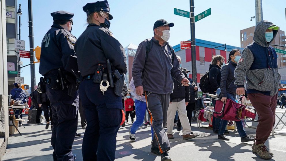 File - Two New York City Police officers patrol a busy intersection on Main Street in Flushing, a largely Asian American neighborhood, Tuesday, March 30, 2021, in the Queens borough, N.Y. More than 26,000 of New York City's municipal workers remained