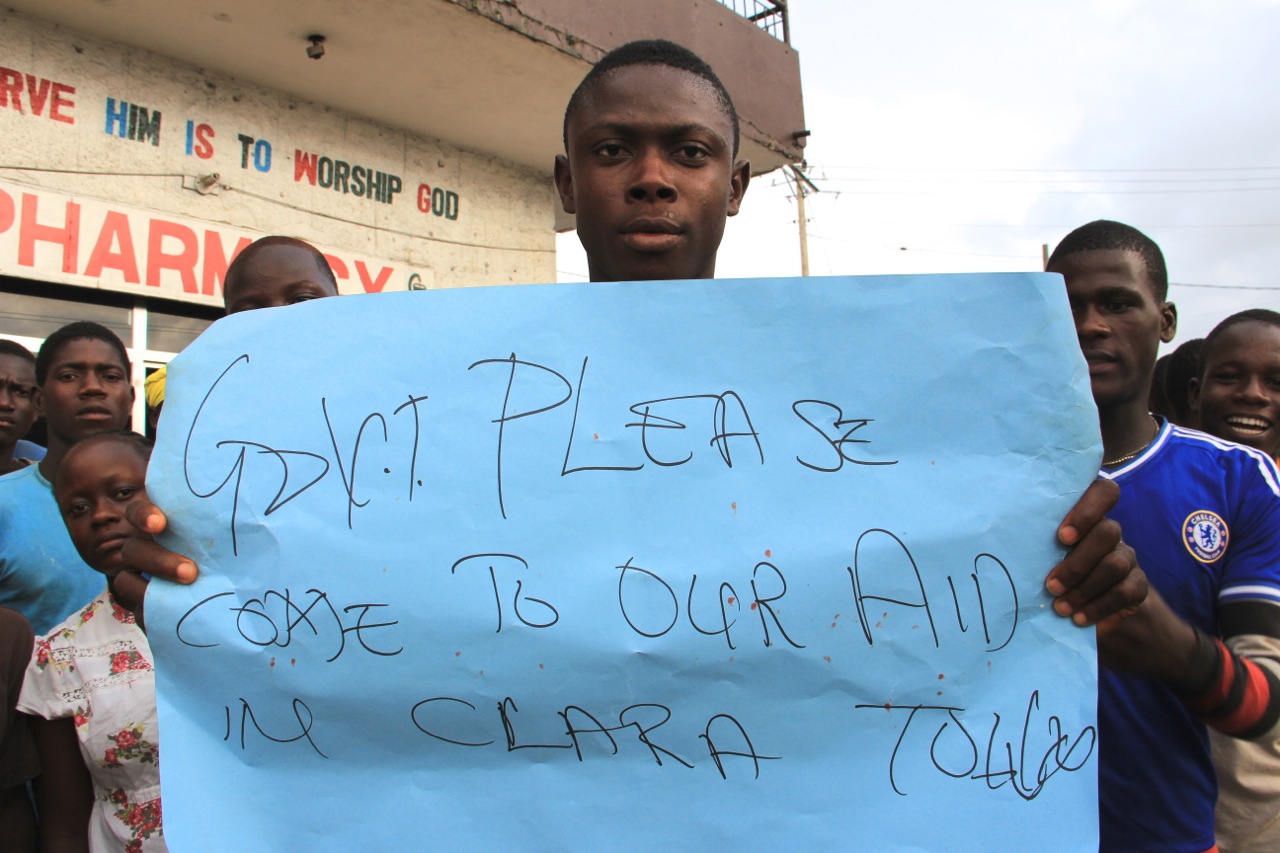 PHOTO: A young man holds a sign at a protest about the delayed removal of a suspected Ebola victim who had died in Clara Town, Liberia, on Thursday. On Saturday morning, community members learned that the dead man's neighbor had also died. 