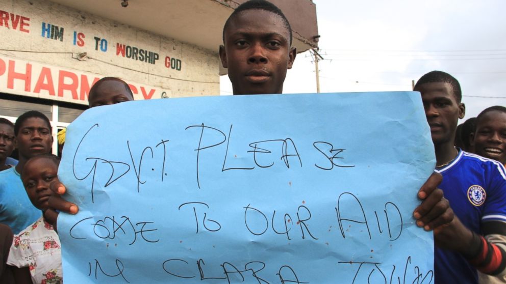 PHOTO: A young man holds a sign at a protest about the delayed removal of a suspected Ebola victim who had died in Clara Town, Liberia, on Thursday. On Saturday morning, community members learned that the dead man's neighbor had also died.