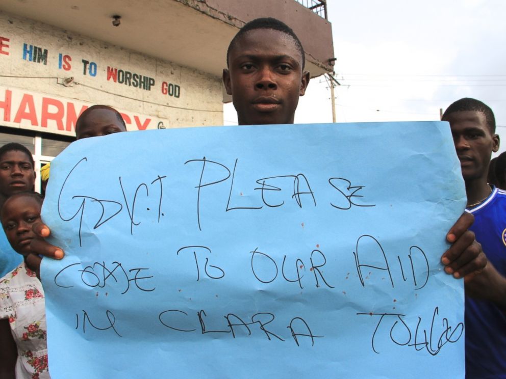 PHOTO: A young man holds a sign at a protest about the delayed removal of a suspected Ebola victim who had died in Clara Town, Liberia, on Thursday. On Saturday morning, community members learned that the dead mans neighbor had also died.