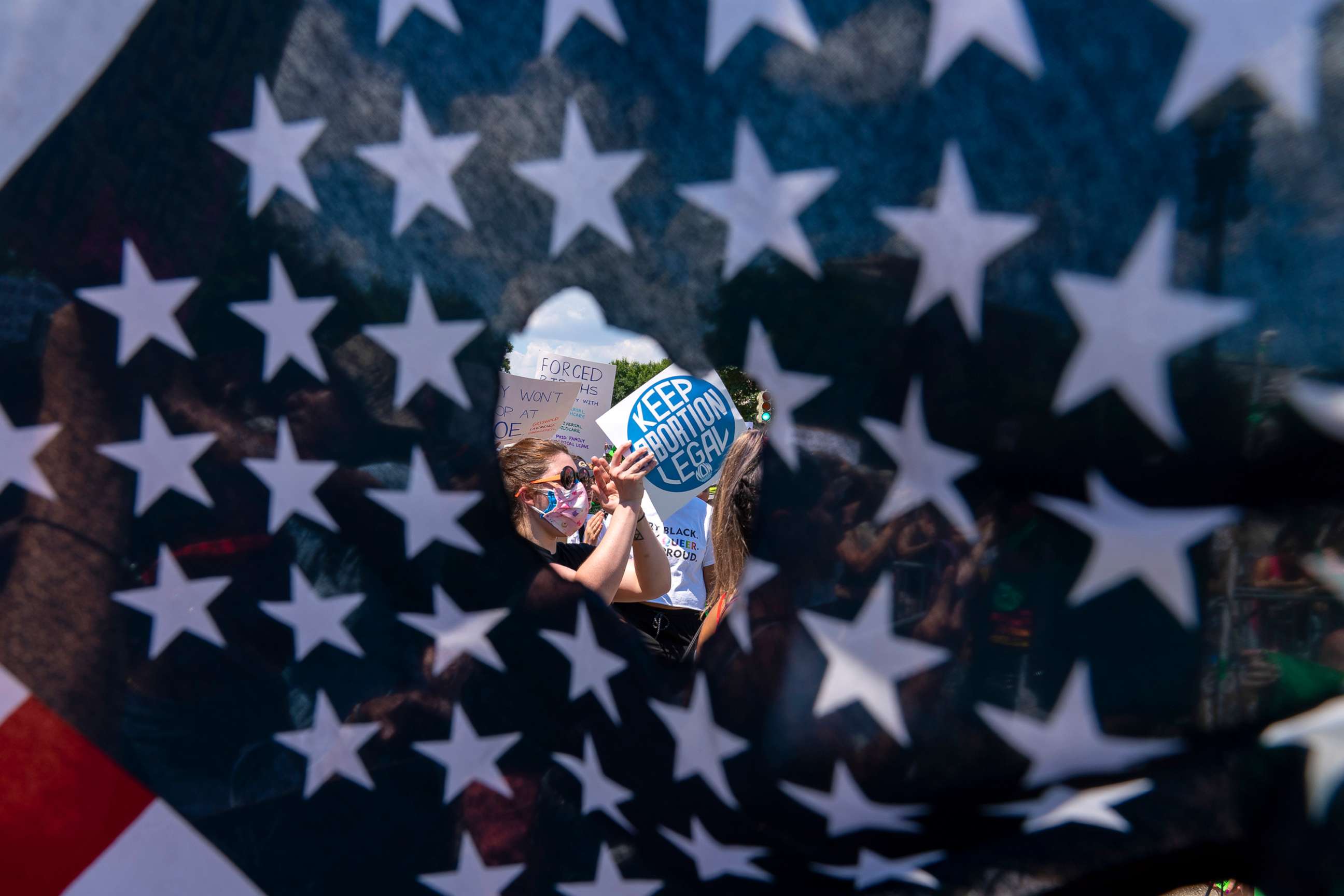 PHOTO: Abortion rights activists are seen through a hole in an American flag as they protest outside the Supreme Court in Washington, June 25, 2022.