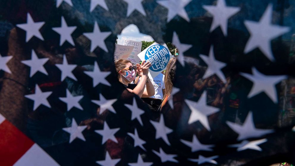 PHOTO: Abortion rights activists are seen through a hole in an American flag as they protest outside the Supreme Court in Washington, June 25, 2022.