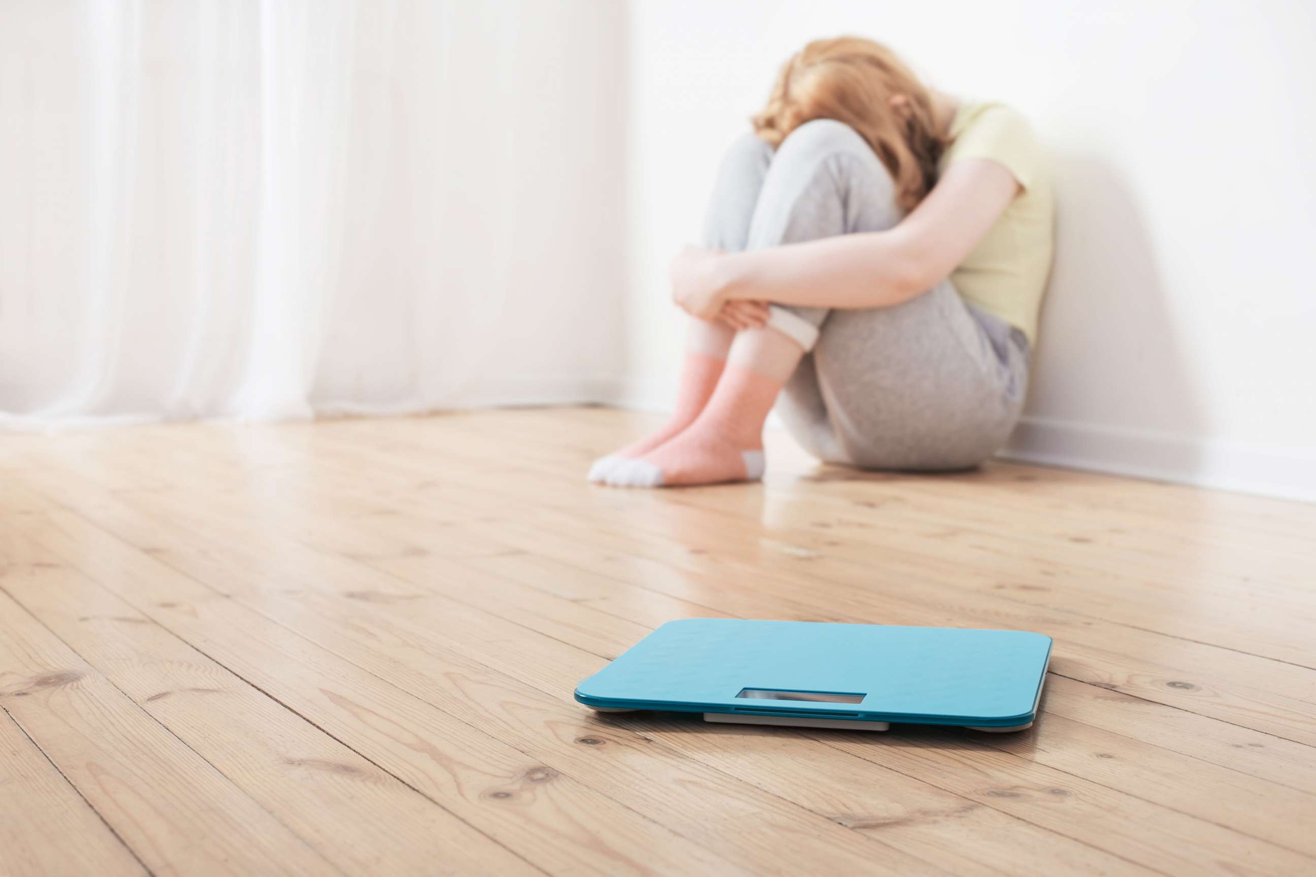 PHOTO: sad teenager girl with scale on wooden floor
