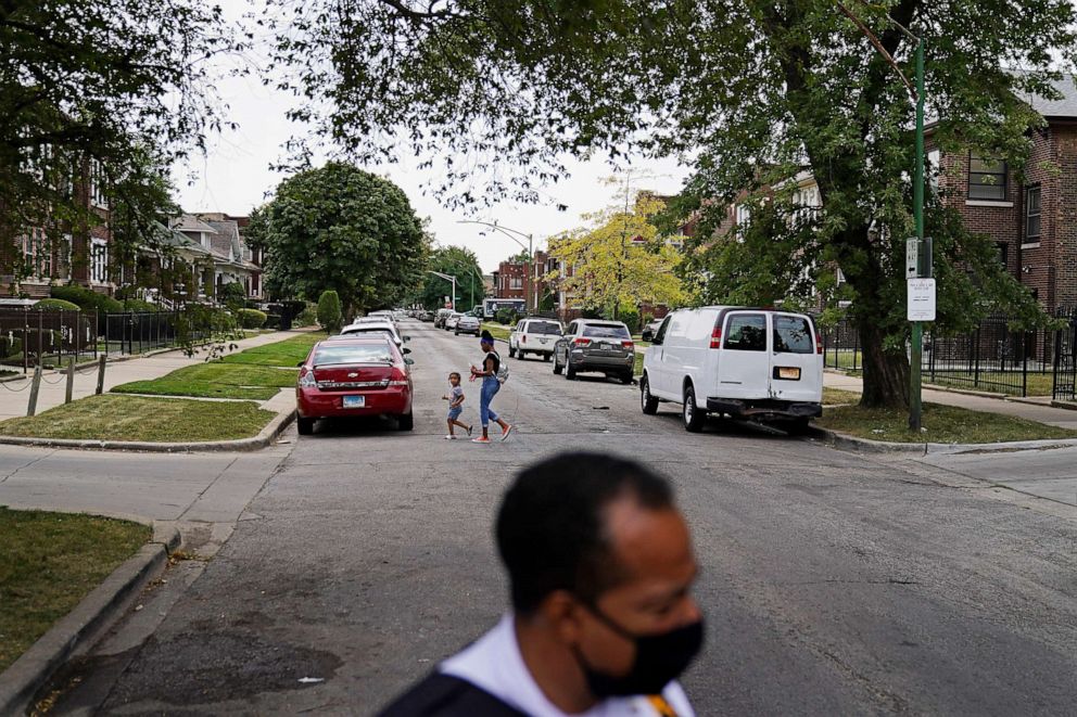 PHOTO: A woman and child cross a street as Police Commander Rahman Muhammad patrols though the Auburn Gresham neighborhood in Chicago, Tuesday, Aug. 25, 2020.