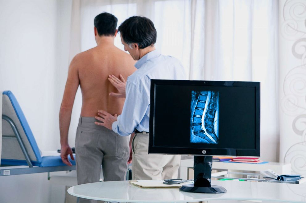 PHOTO: A doctor examines a patients back behind an MRI of a lumbar disc herniation.