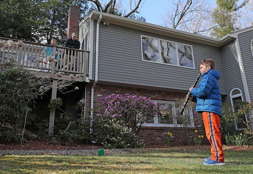 PHOTO: In this April 11, 2020, file photo, Gabriel Waller plays his clarinet for his grandparents Josie and Lew Schneider from a safe distance instead of a visit inside their home due to the coronavirus pandemic in Newton, Mass.