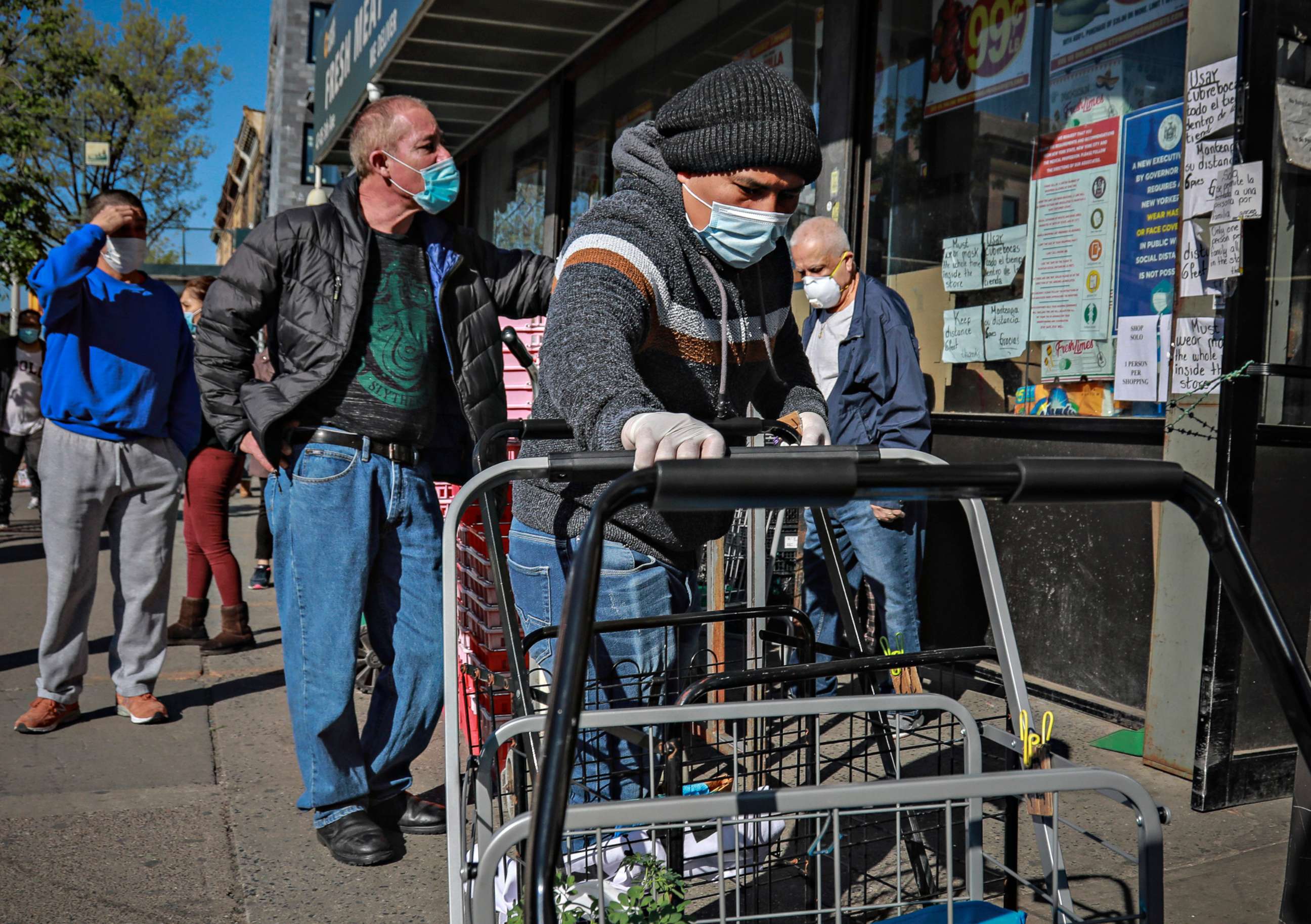 PHOTO: A masked grocery store worker in Brooklyn's Sunset Park neighborhood with one of the city's largest Mexican and Hispanic community, organize shopping carts while people waiting to enter the store, May 5, 2020, in New York City.