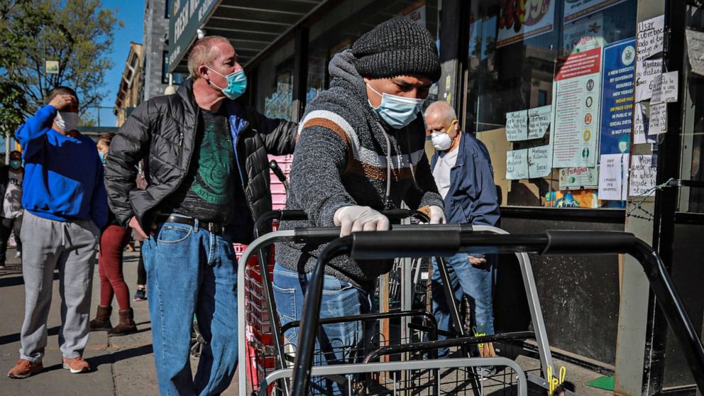 PHOTO: A masked grocery store worker in Brooklyn's Sunset Park neighborhood with one of the city's largest Mexican and Hispanic community, organize shopping carts while people waiting to enter the store, May 5, 2020, in New York City.