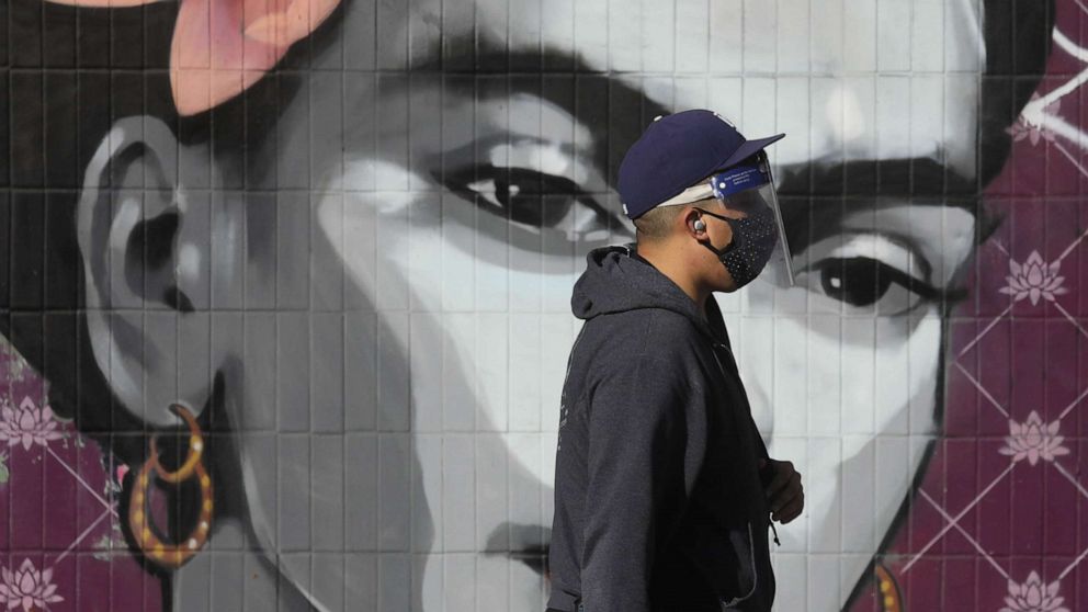 PHOTO: A pedestrian wearing a protective mask and face shield passes in front of a mural of artist Frida Khalo in the Echo Park neighborhood of Los Angeles, Dec. 3, 2020. 