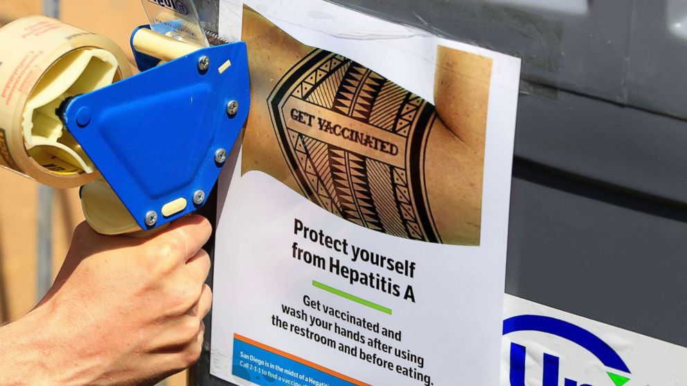 PHOTO: A worker tapes signage telling people to get vaccinated to protect themselves against hepatitis A on hand washing sinks installed at the Neil Good Day Center in downtown San Diego, Sept. 1, 2017.