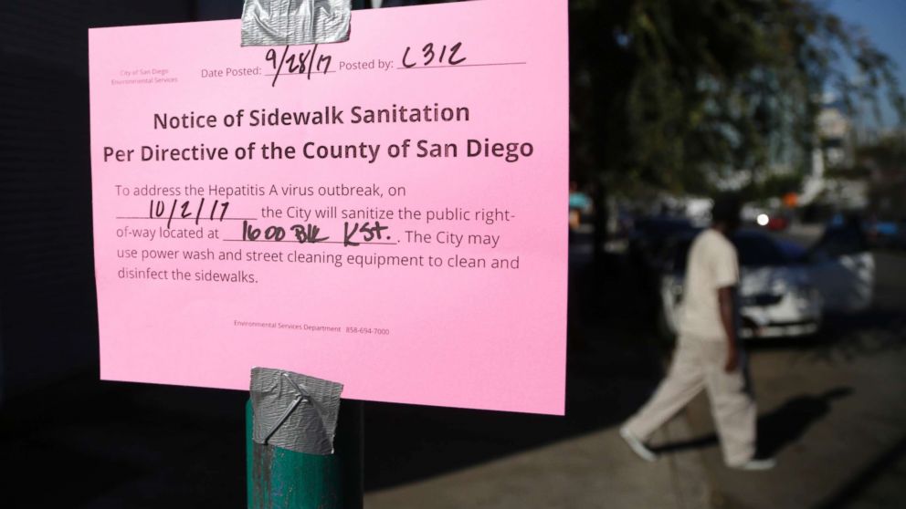 PHOTO: A man passes behind a sign warning of an upcoming street cleaning to address a hepatitis A outbreak in San Diego, Sept. 28, 2017.
