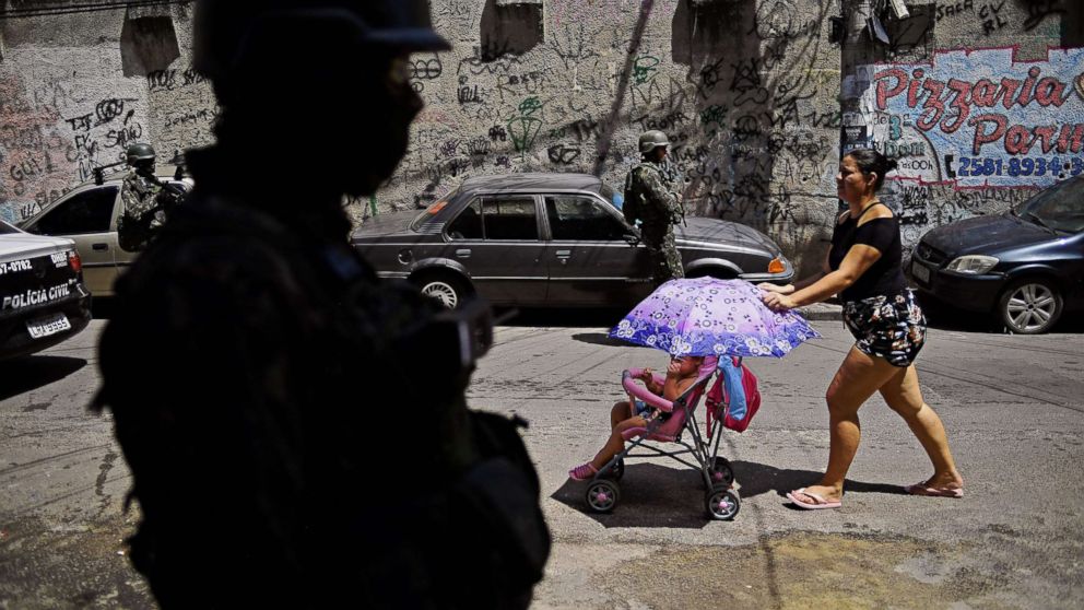 PHOTO: A woman walks past Brazilian military on patrol in Jacarezinho favela in Rio de Janeiro on Jan. 18, 2018. 