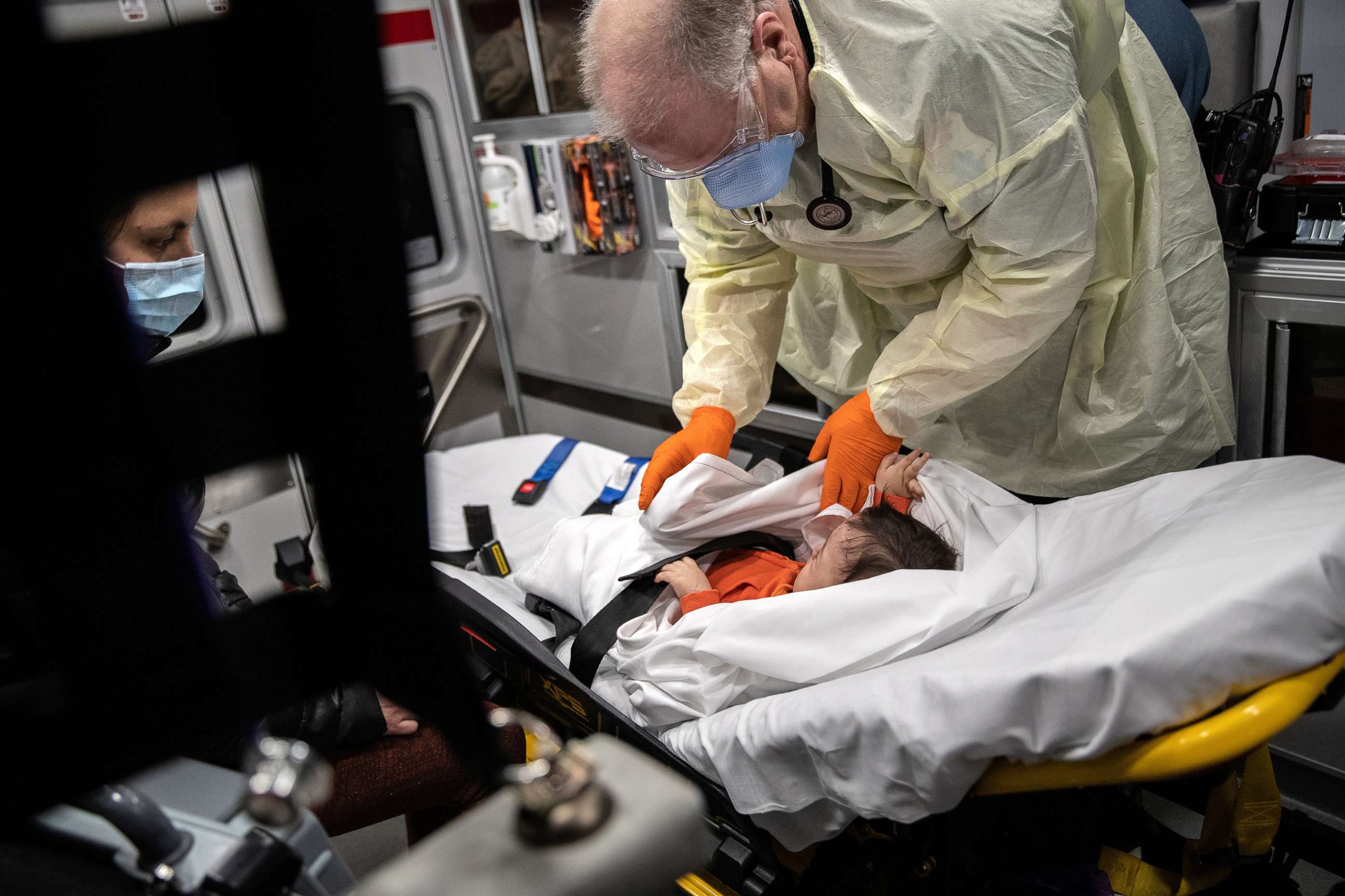 PHOTO: In this April 4, 2020, file photo, a paramedic wearing personal protection equipment (PPE), tends to a 10-month-old boy with fever while riding by ambulance with the infant's mother to Stamford Hospital in Stamford, Conn.