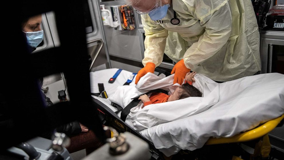 PHOTO: Paramedic Randy Lilly, wearing personal protection equipment (PPE), tends to a 10-month-old boy with fever while riding by ambulance with the infant's mother to Stamford Hospital, April 4, 2020, in Stamford, Conn.