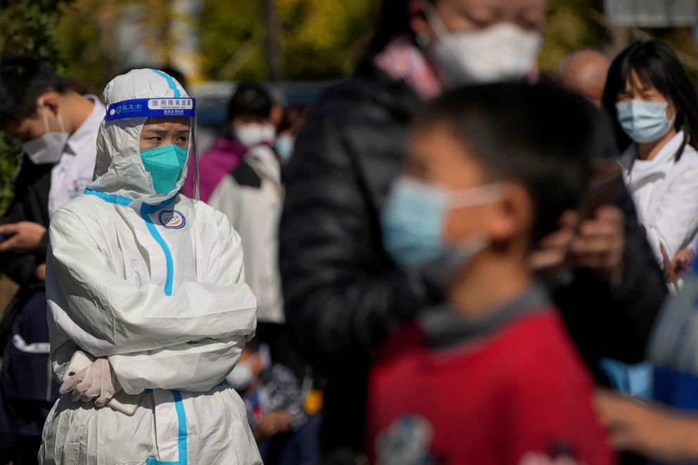 PHOTO: A worker in protective suit stands watch as masked residents wait in line to get their routine COVID-19 throat swabs tests at a coronavirus testing site in Beijing, Oct. 18, 2022.