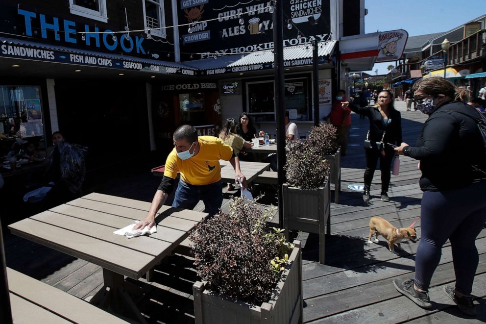 PHOTO: A man wears a face mask while cleaning an outdoor dining table at Pier 39 where some stores, restaurants and attractions have reopened during the coronavirus outbreak in San Francisco, June 18, 2020.