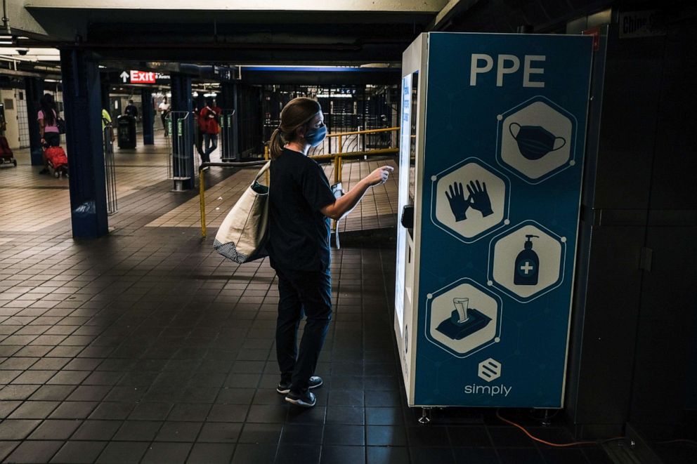 PHOTO: A woman uses a personal protective equipment vending machine that was recently deployed by the Metropolitan Transportation Authority in the 42nd Street Port Authority Bus Terminal subway stop on June 30, 2020, in New York.
