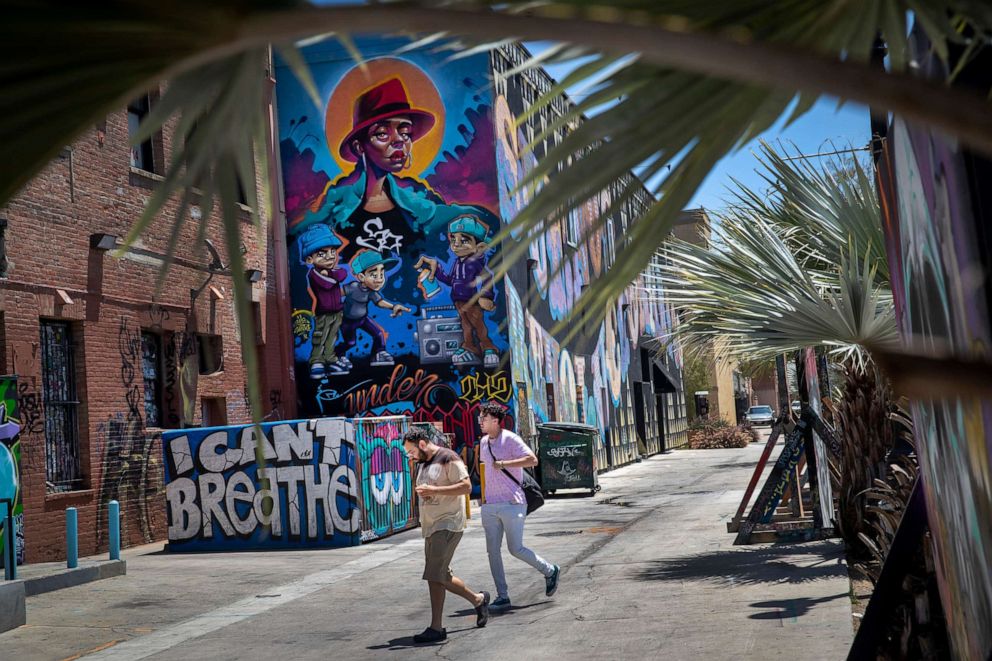 PHOTO: Pedestrians not wearing masks walk past murals in downtown Santa Ana, Calif., July 7, 2020.