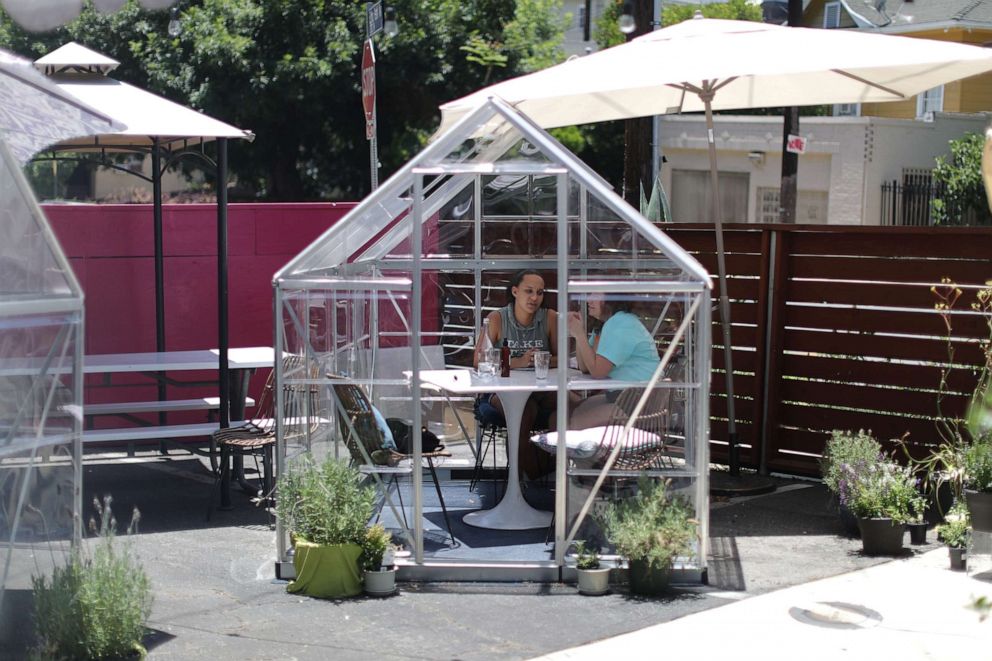 PHOTO: Nuria Bosch, 29, and Dria Abramson, 29, eat lunch in a social distancing greenhouse dining pod set up in the former parking lot of the Lady Byrd Cafe in Los Angeles, July 7, 2020.