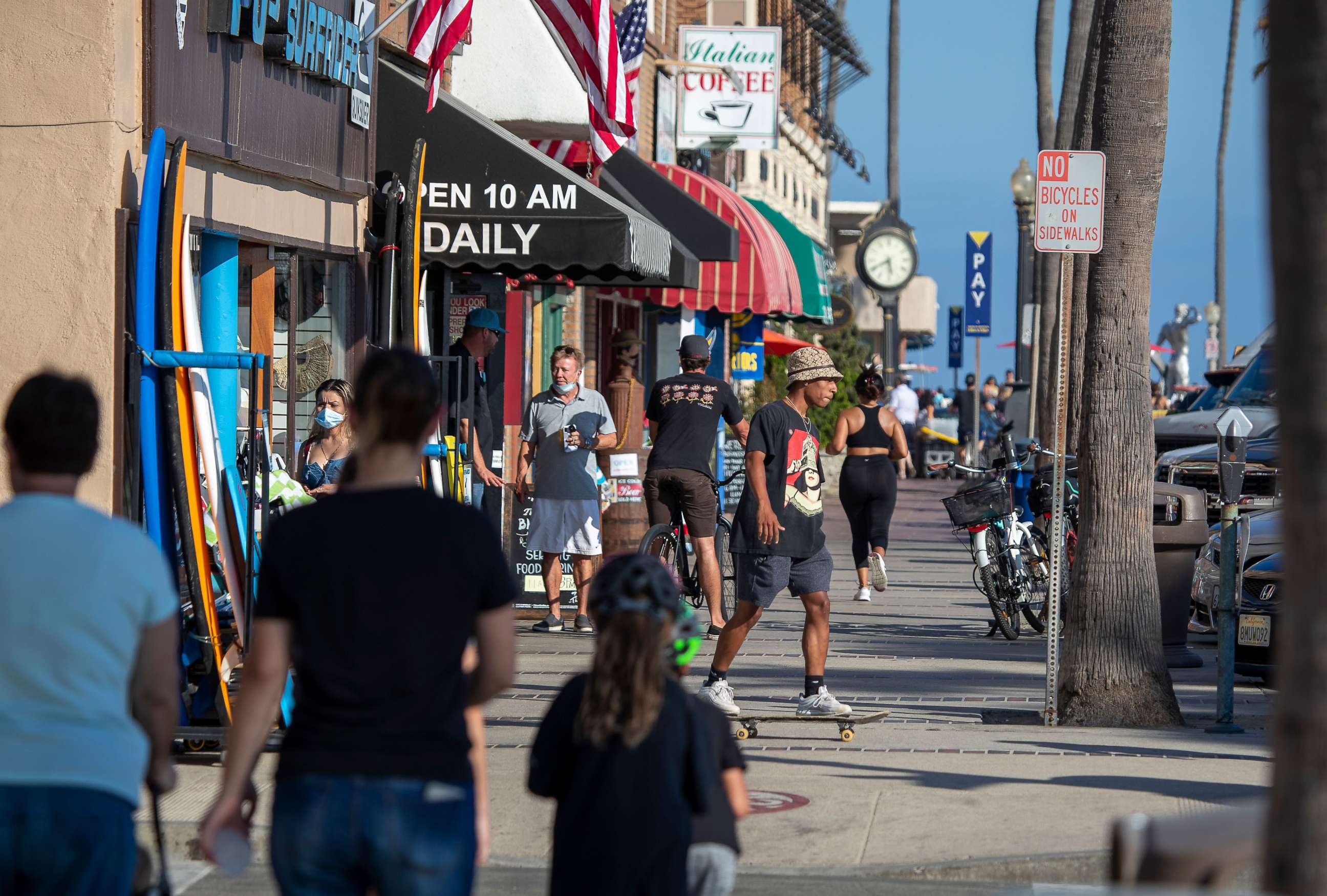 PHOTO: People walk and skateboard on the sidewalk past businesses on July 20, 2020, in Newport Beach, Calif.