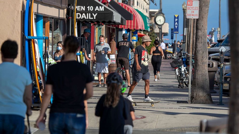 PHOTO: People walk and skateboard on the sidewalk past businesses on July 20, 2020, in Newport Beach, Calif.